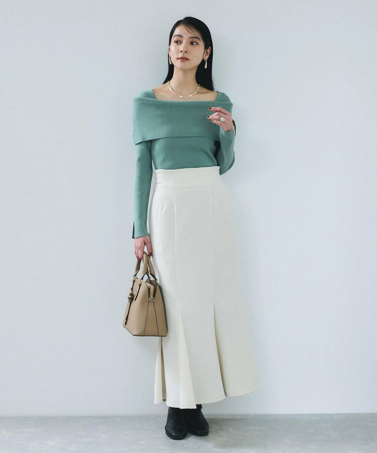 ミントグリーンのニットに白スカートを合わせた女性
