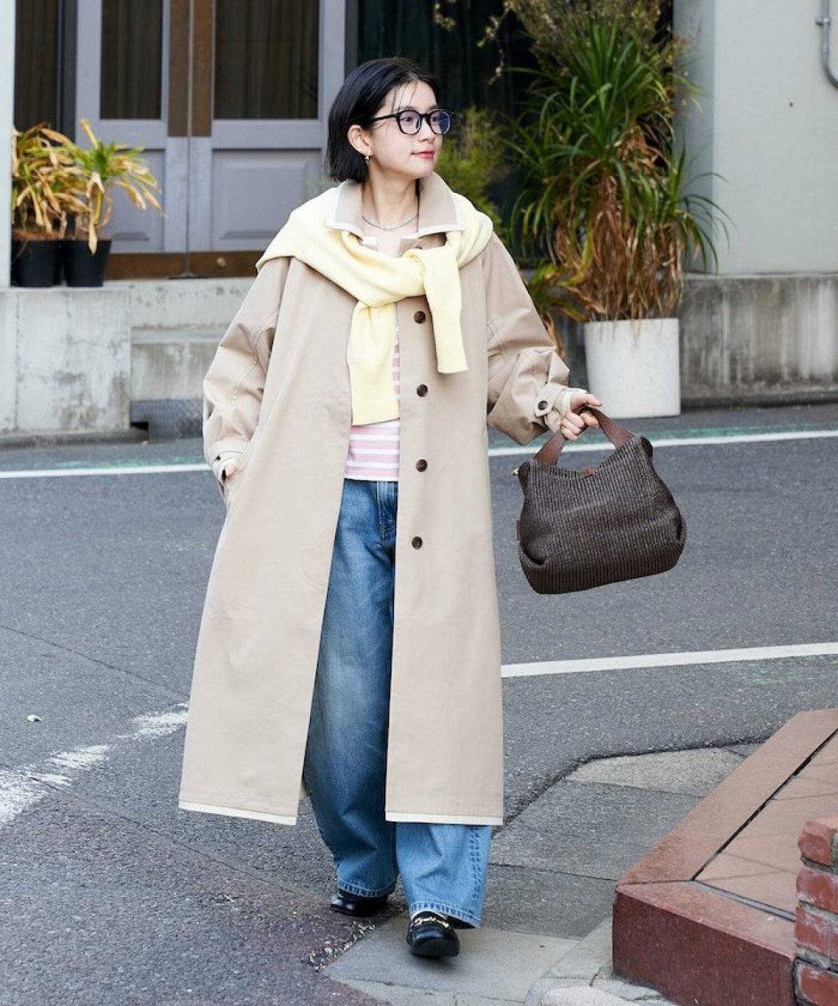 ネイビーのスウェットにデニムを合わせてベージュのアウターを羽織った女性