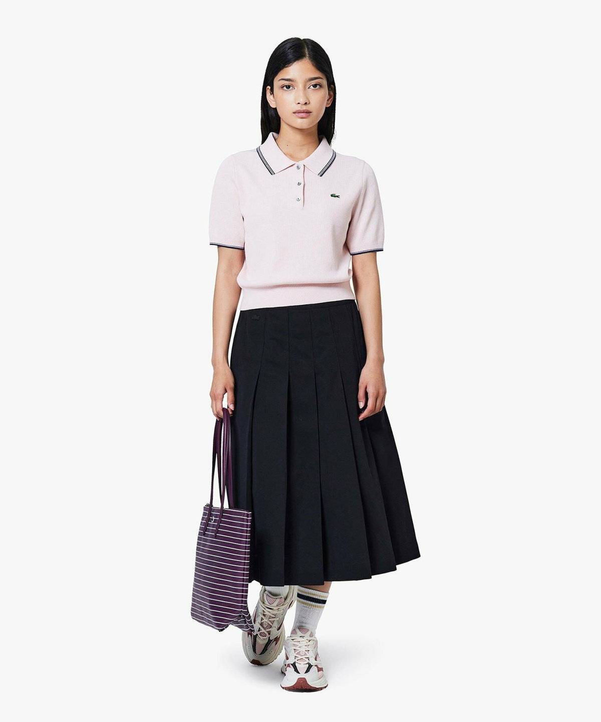 ピンクのポロシャツに黒のプリーツスカートを合わせた女性