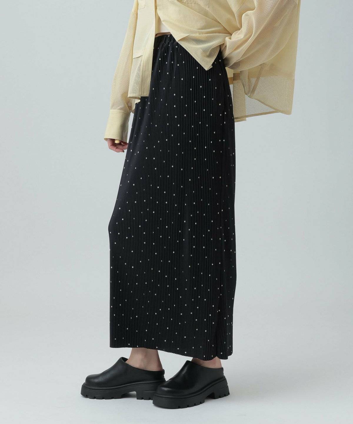 グリーンのブラウスに黒のプリーツスカートを合わせた女性