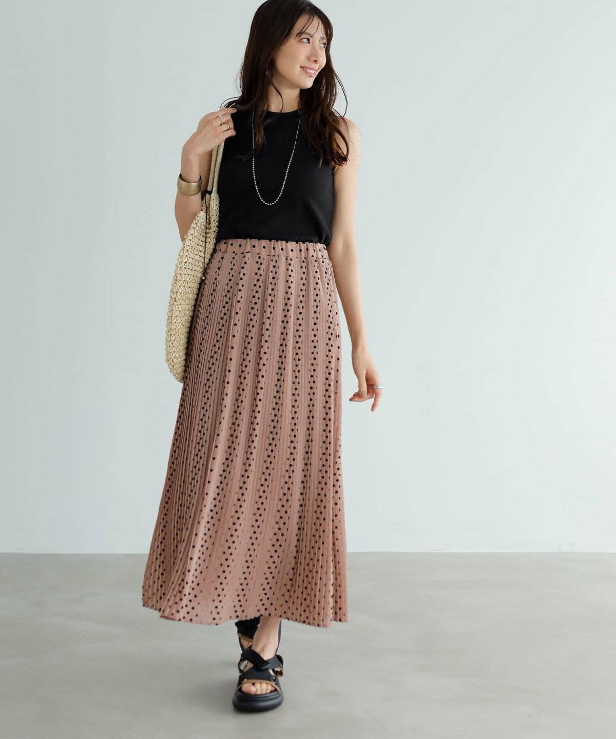 サマーニットにドット柄のプリーツスカートを合わせた女性