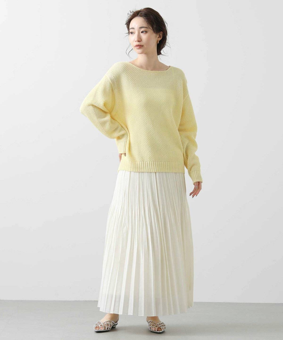 イエローのカーディガンに白のプリーツスカートを合わせた女性