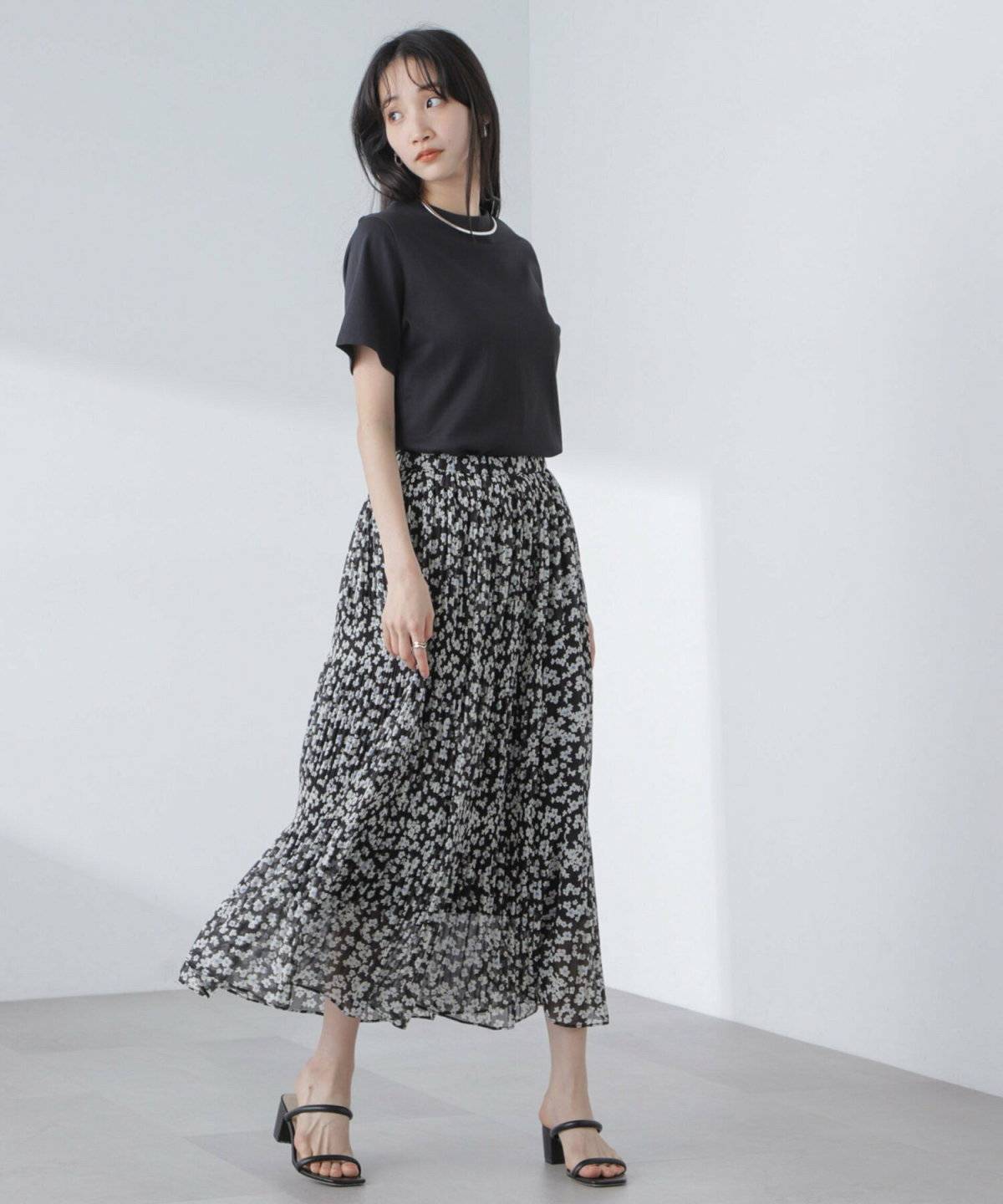 黒Tシャツに花柄のプリーツスカートを合わせた女性