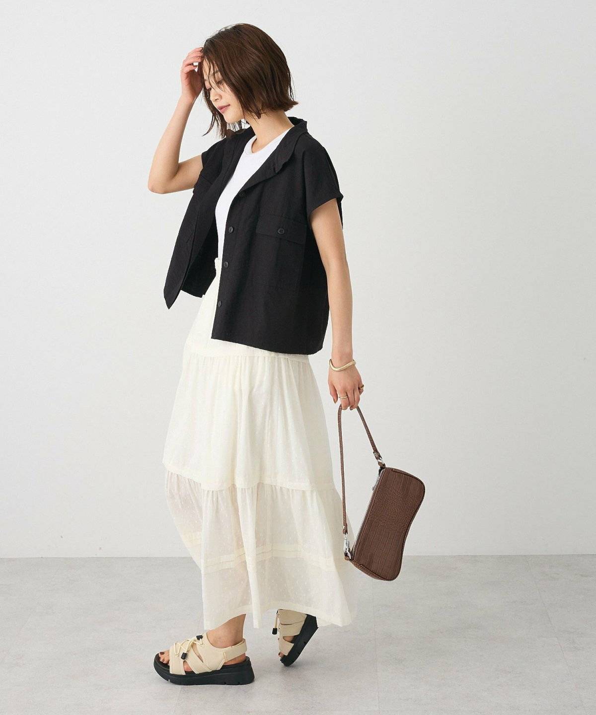 ボーダー柄のトップスに白スカートを合わせて黒ベストを重ねた女性