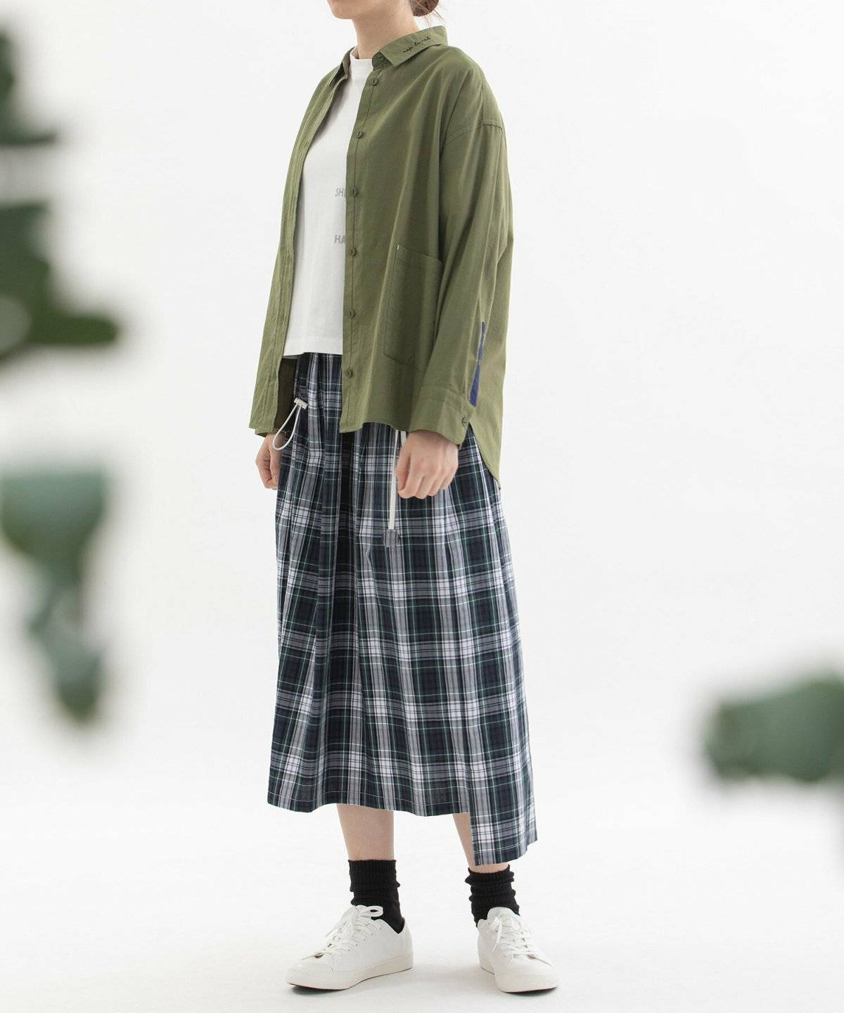 黒ニットにチェック柄スカートを合わせてグリーンのシャツを羽織った女性