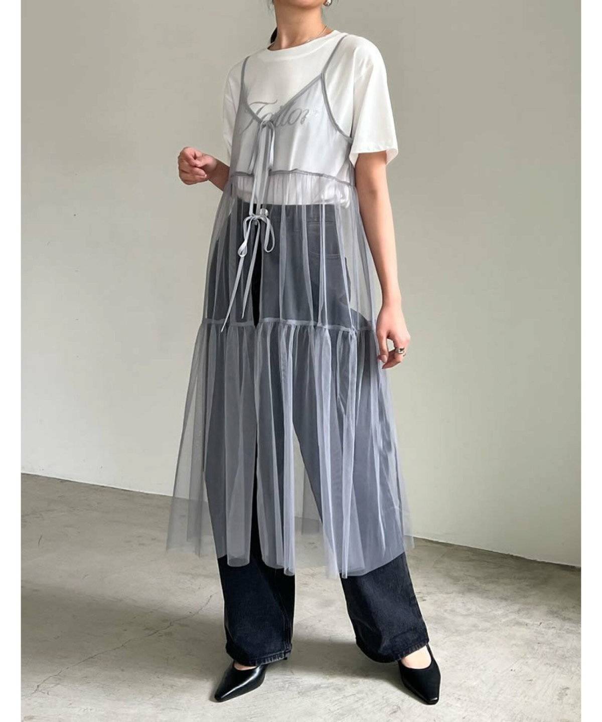 ロゴTシャツにデニムをはいてキャミワンピースを重ねた女性