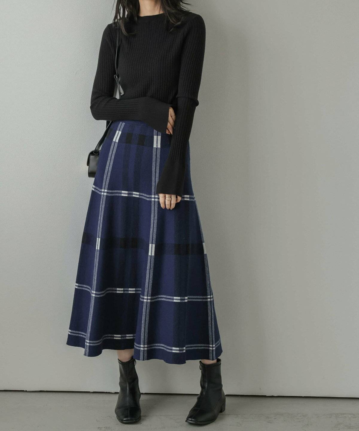 黒ニットにブルーのチェック柄スカートを合わせた女性