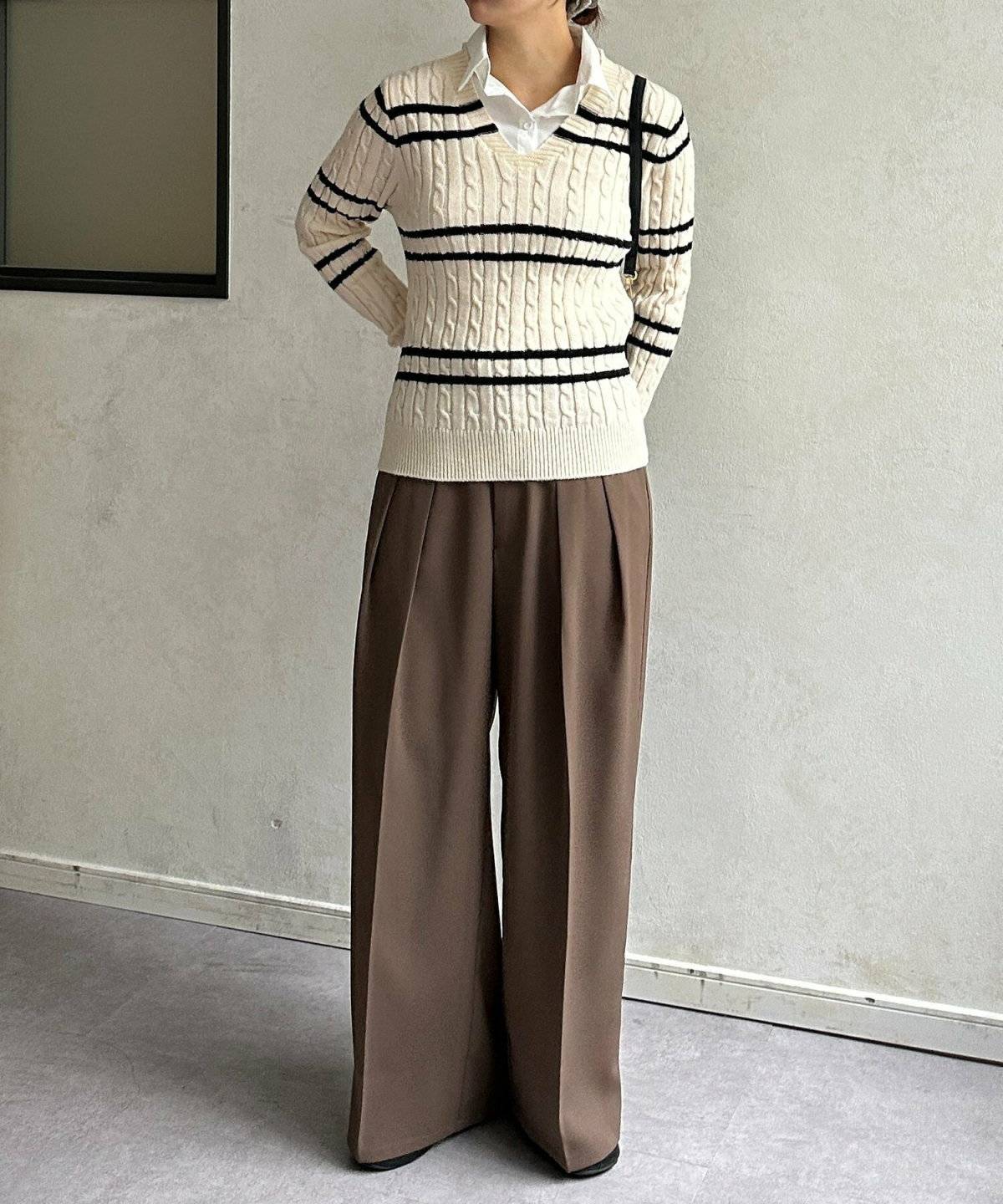 グリーンのニットにブラウンのパンツを合わせた女性