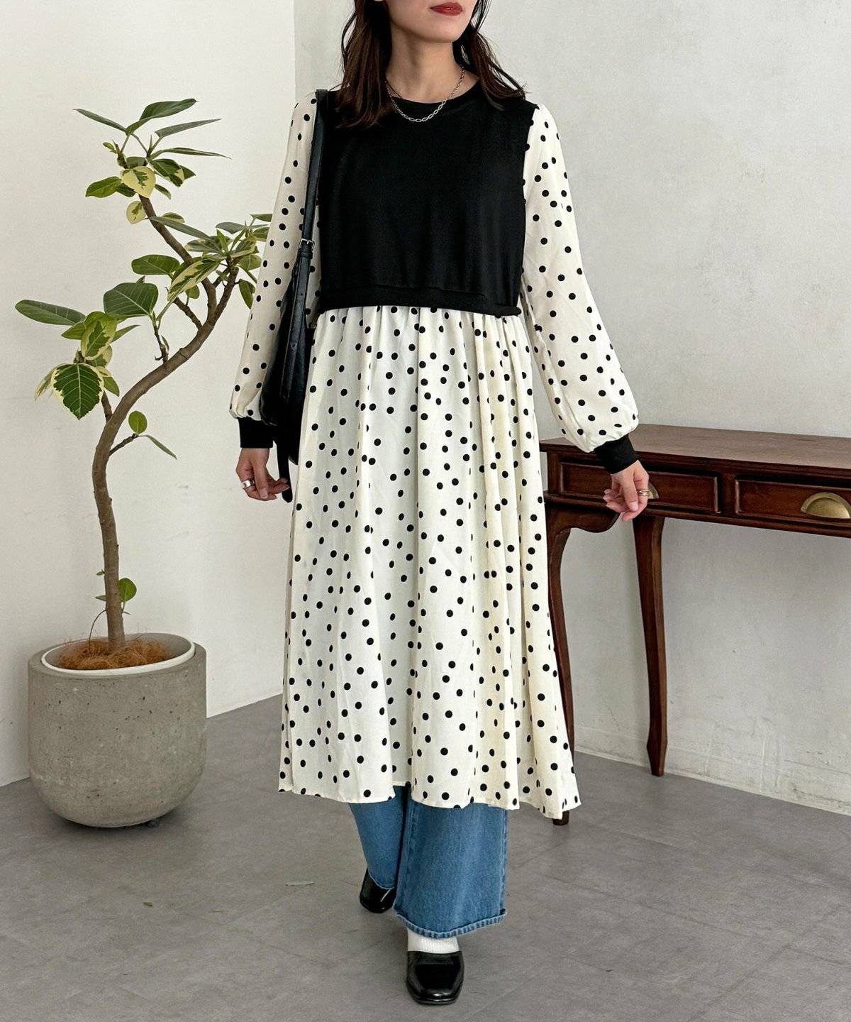 ドット柄ワンピースにニットベストを重ねた女性