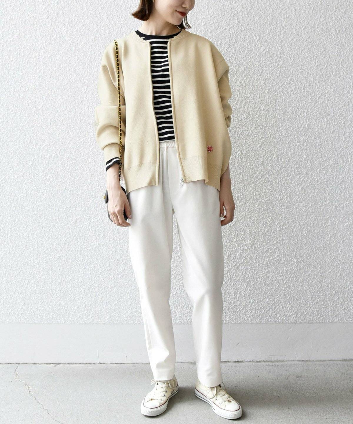 ボーダー柄のキャミソールにベージュのブルゾンを羽織って白パンツを穿いた女性