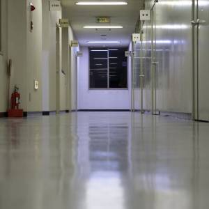  夜の会社の廊下に並ぶ部屋の扉と、突き当たりの窓 