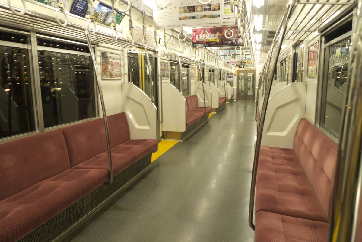 赤い座席とつり革が並ぶ、夜の空いた電車の車内