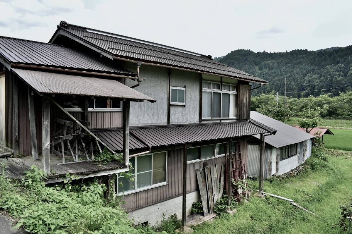 草の伸びた庭先に建つ、古い木造の家
