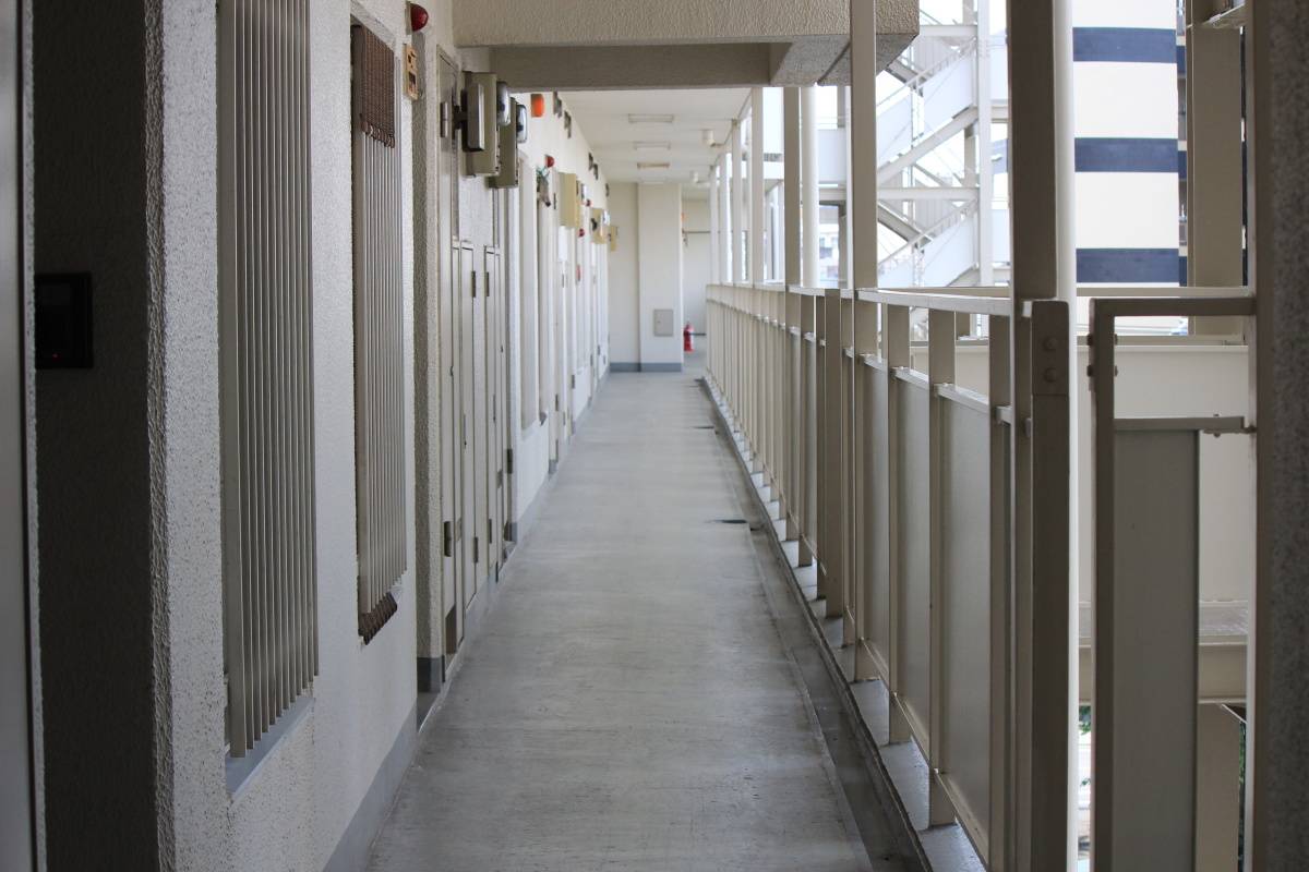 マンションの共用廊下が奥まで一直線に続き、玄関ドアが並んでいる通路の昼間の風景