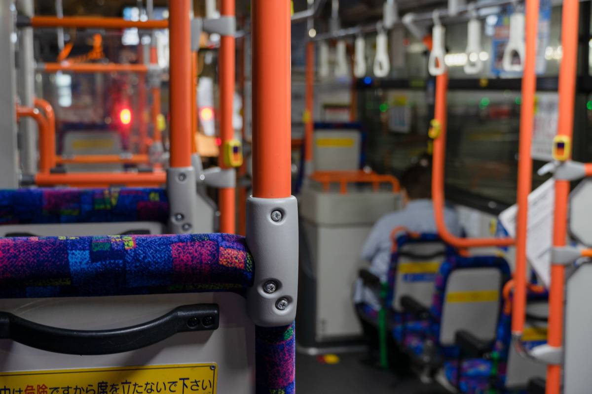 オレンジ色の手すりと吊り革が並ぶ路線バスの車内。座席や降車ボタンが見える。