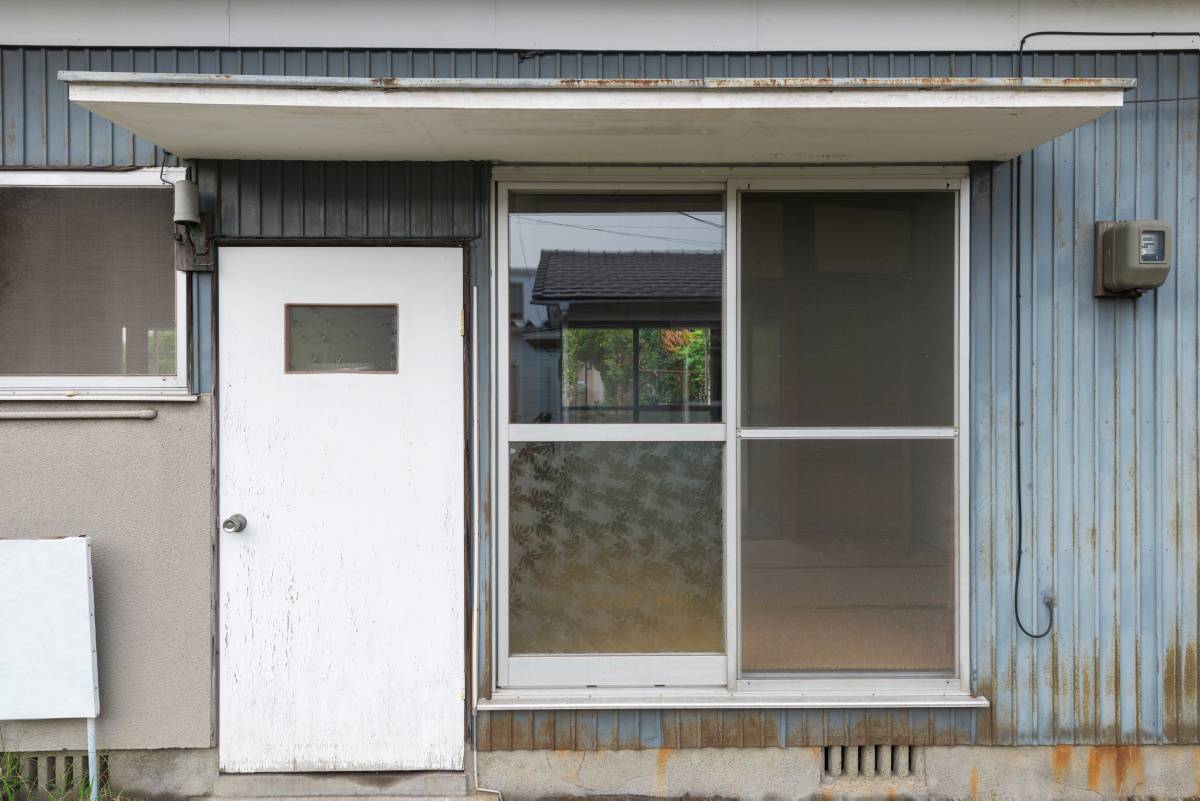 古い空き家。大きい扉の横に窓がある外観。