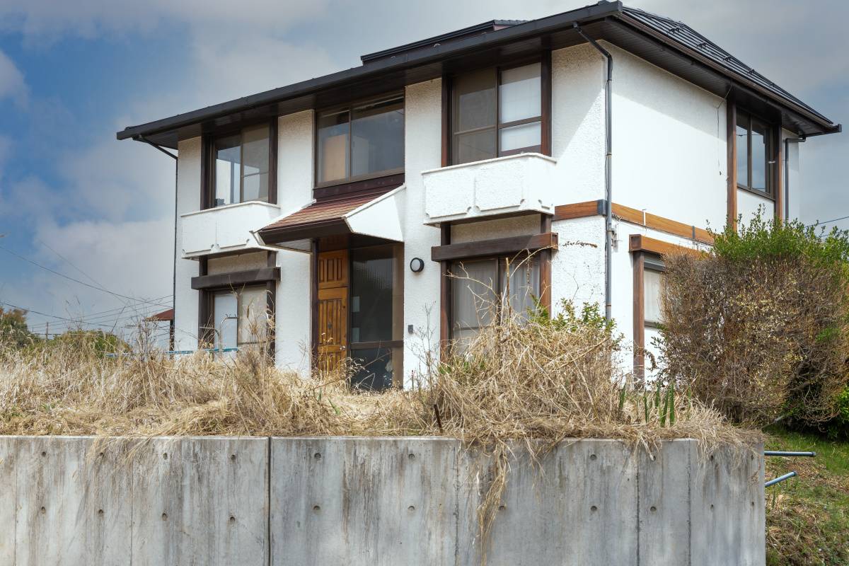 草が生い茂る庭に囲まれた、白い壁の古い二階建て一軒家