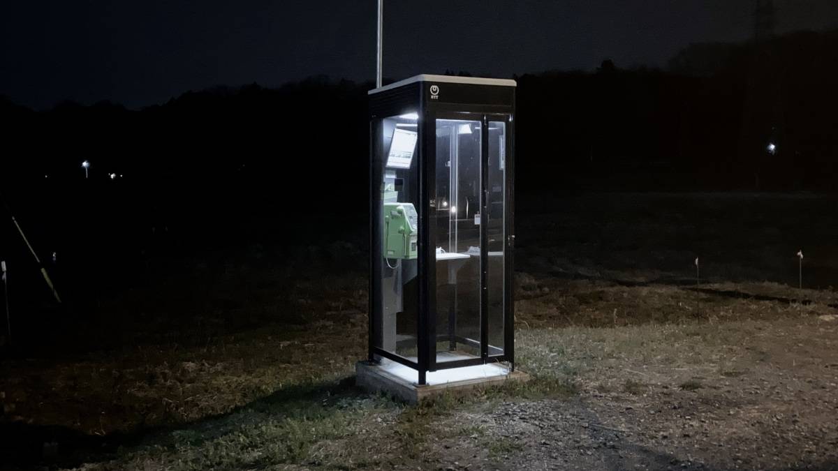暗い夜道にぽつんと立つ、明かりのついた公衆電話ボックス。