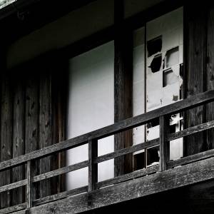  古びた木造建物の外観。木製の手すりの奥に、破れた障子が並んでいる。 