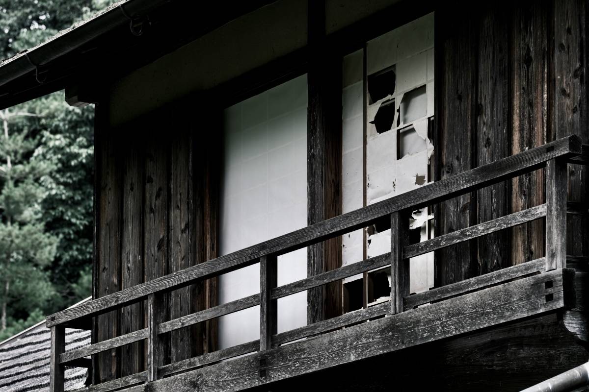 古びた木造建物の外観。木製の手すりの奥に、破れた障子が並んでいる。